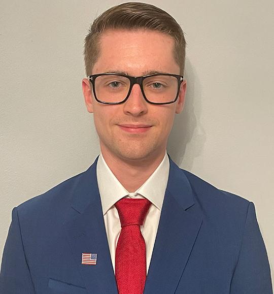 headshot of young man with coat and tie, glasses